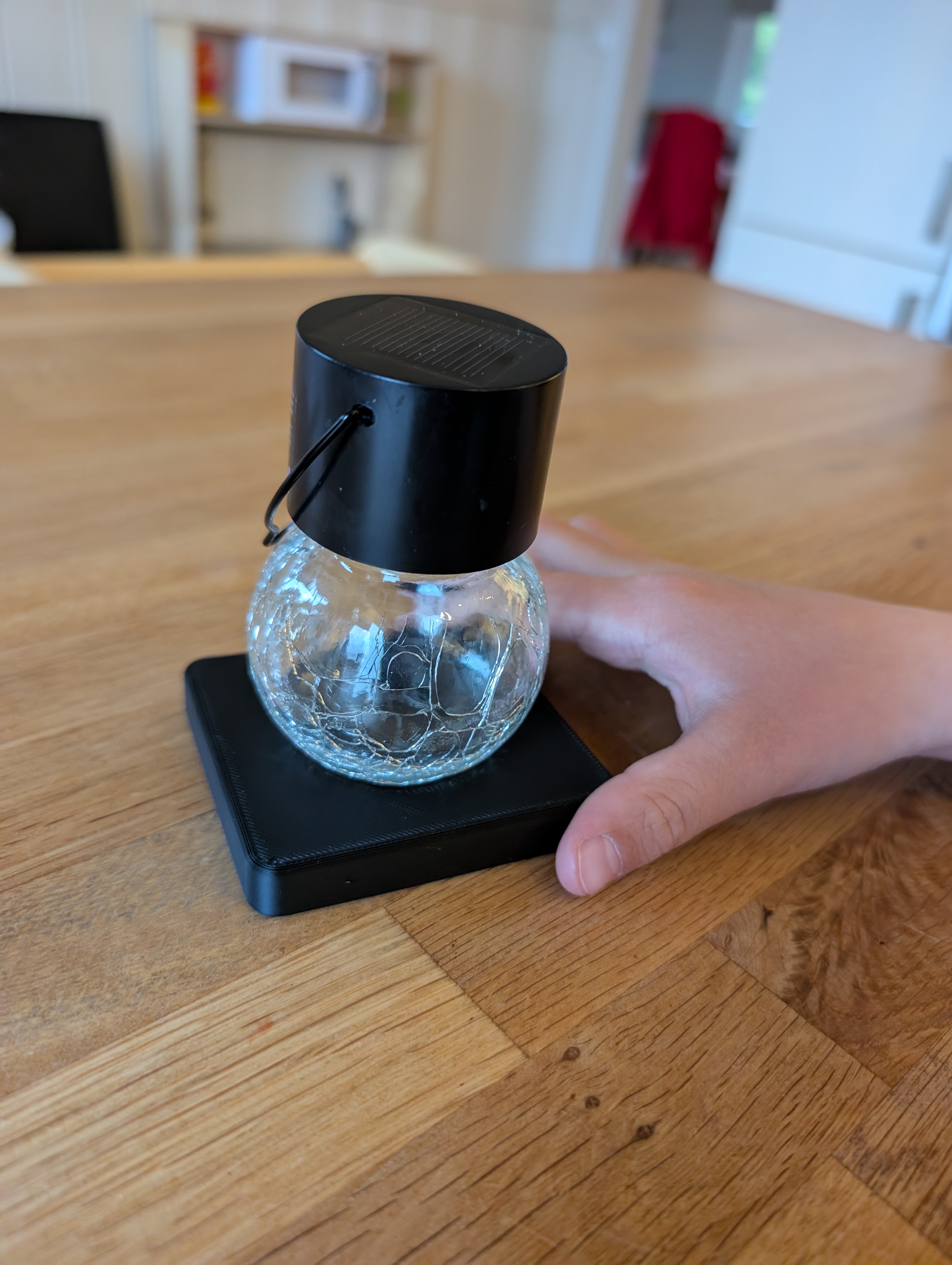 A small solar light bulb sitting in a compact black 3D-printed desk stand on a wooden table.